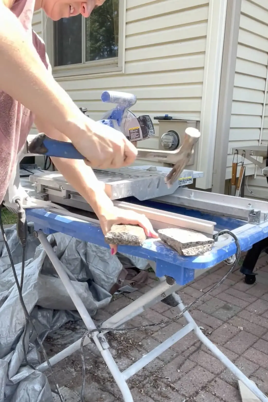 Close-up of woman breaking a stone veneer piece with a hammer on a workbench after cutting.